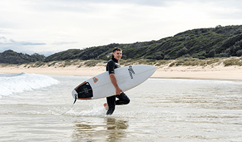 A male with a surfboard exits the water at Cape Conran Coastal Park